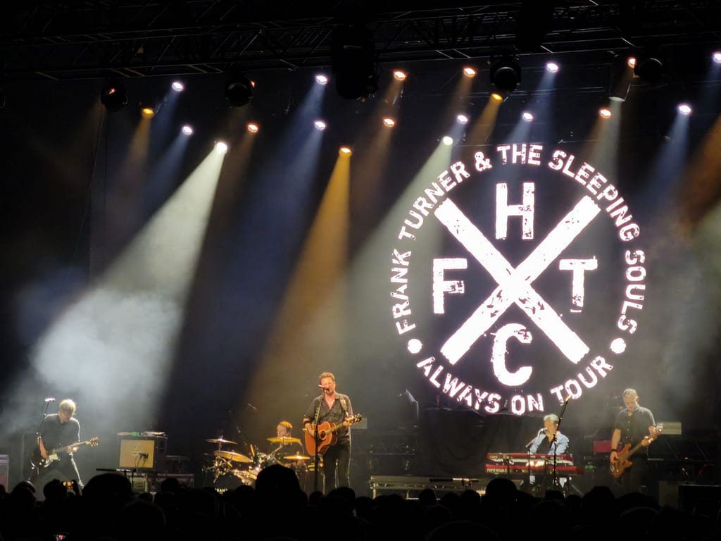 Frank Turner and the Sleeping Souls auf der Bühne vor dem Bendschriftzug und dem FTHC-Cross (Frank Turner Hardcore)