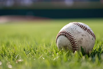 Rasen in Makroaufnahme, in der rechten Hälfte liegt ein dreckiger Baseball